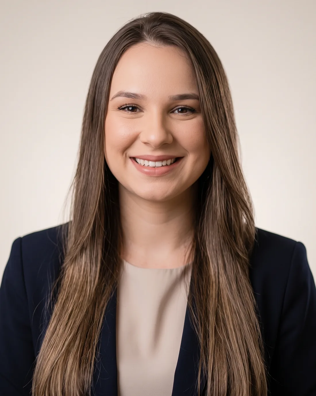 Suyenne Amaral sorrindo, de blazer azul escuro e blusa clara, em retrato frontal sobre fundo claro